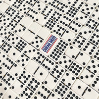A close-up overhead view of many white domino tiles with black pips, arranged in a grid. One central domino is different, with the words "Cuban Bred" printed in blue and red.