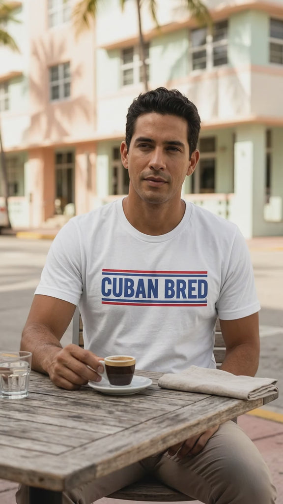 Video of a man at an outdoor café table in Miami Beach's Art Deco district enjoying Cuban espresso, wearing a white Cuban Bred™ graphic t-shirt – Cuban American graphic tee, Miami gift by Martha of Miami