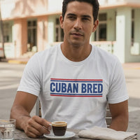 Video of a man at an outdoor café table in Miami Beach's Art Deco district enjoying Cuban espresso, wearing a white Cuban Bred™ graphic t-shirt – Cuban American graphic tee, Miami gift by Martha of Miami