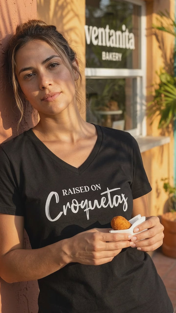 Video of a woman outside a Cuban ventanita bakery window holding a croqueta, wearing a black Raised on Croquetas women's v-neck t-shirt – Cuban American graphic tee, Miami gift by Martha of Miami